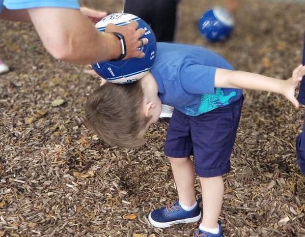 Teacher teaching a young little boy how to balance a soccer ball behind his head on their soccer activity at a Preschool & Daycare Serving Hampton Roads, VA