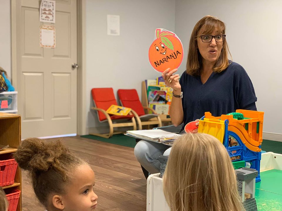 Teacher showing the preschool kids a Naranja (Spanish) picture on her hands which means Orange fruit in English at a Preschool & Daycare Serving Hampton Roads, VA