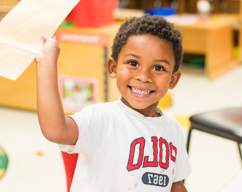 Happy african american nursery boy raising his hands while holding a paper at a Preschool & Daycare Serving Hampton Roads, VA